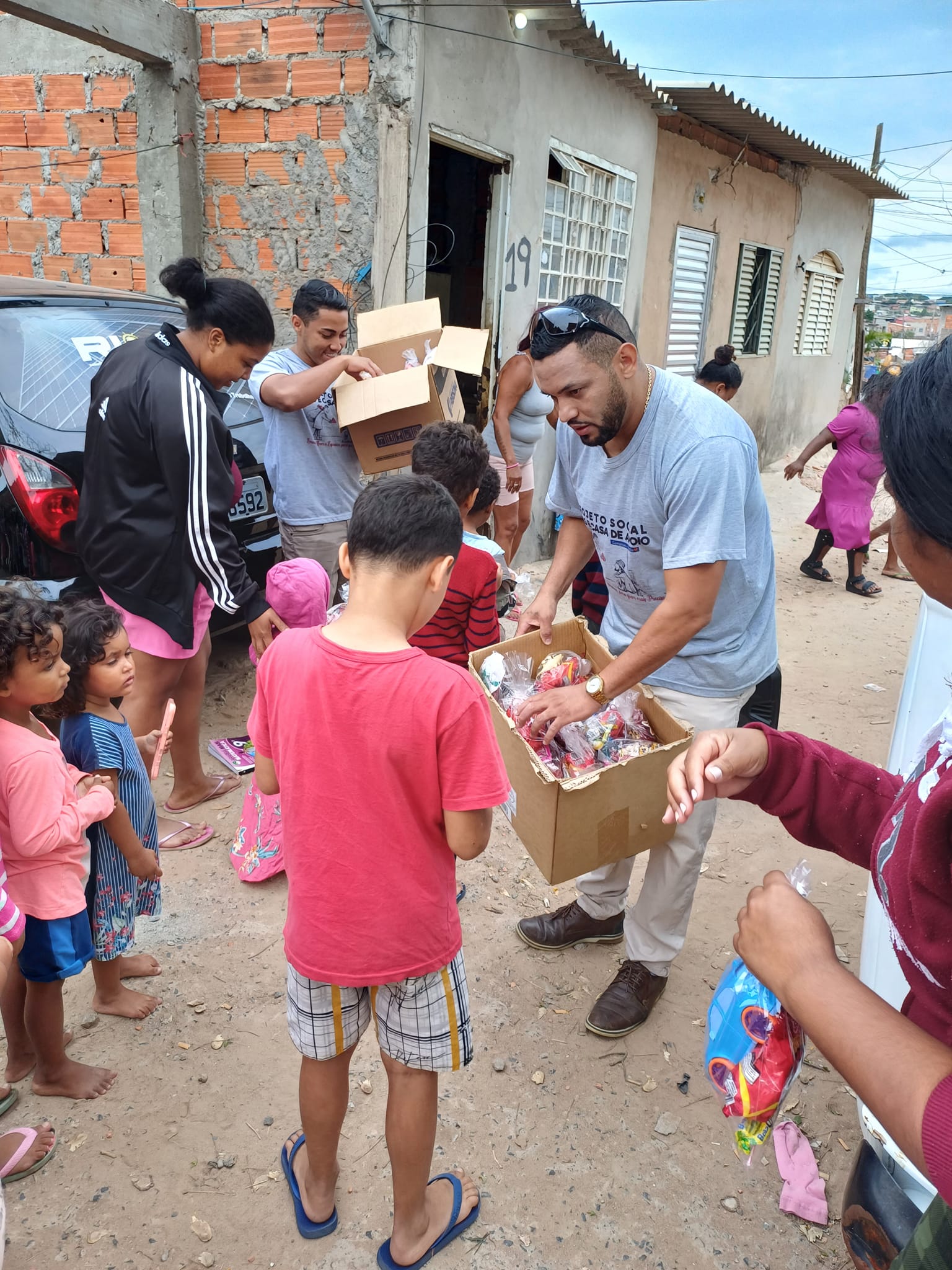Voluntários da ONG entregando kits e doces a crianças em comunidade de Campinas